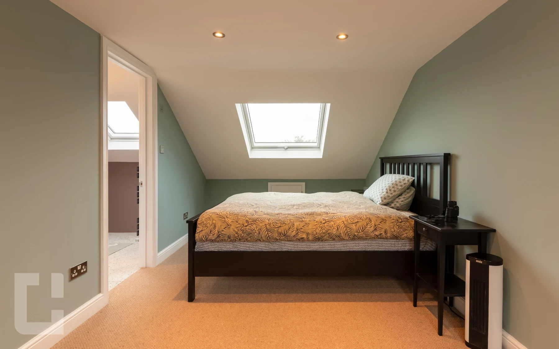 Sage green loft bedroom with a double bed beneath a Velux rooflight in the sloping ceiling