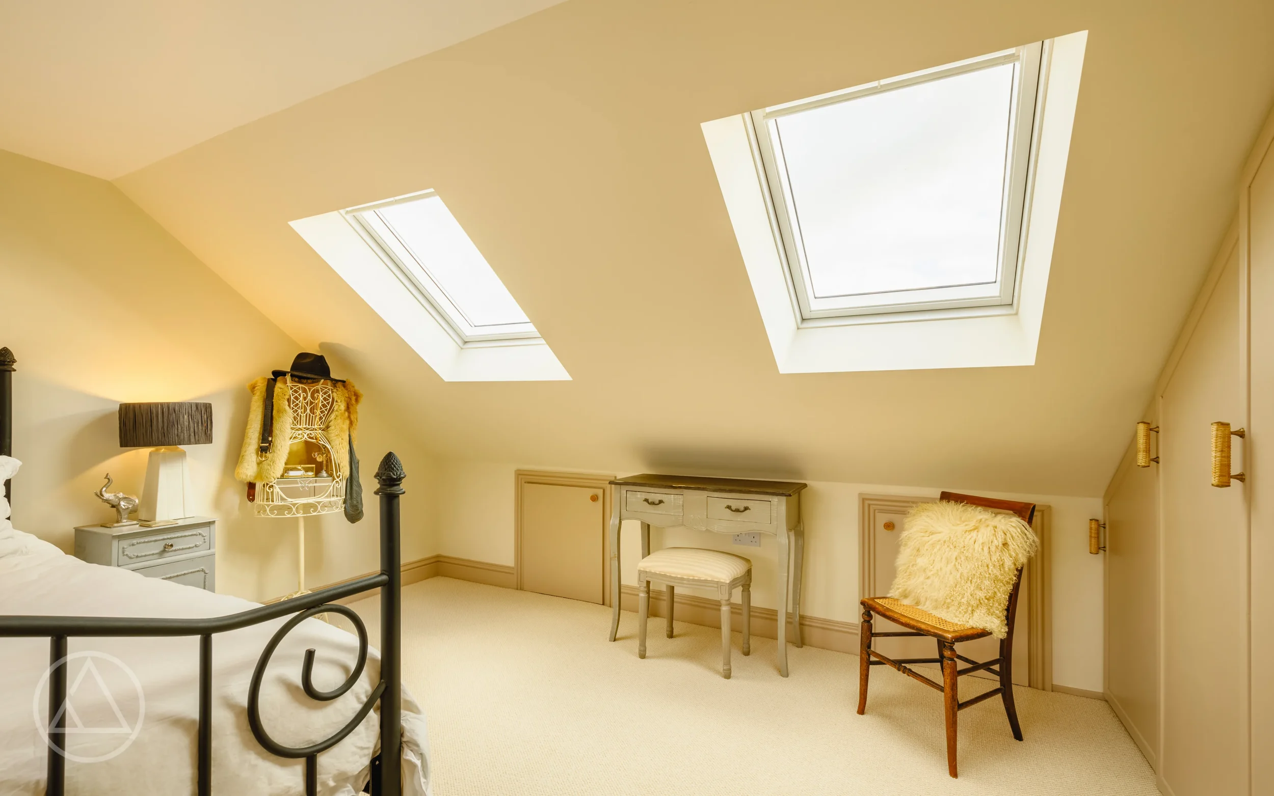 Loft bedroom with a painted dressing table and stool below two large rooflights