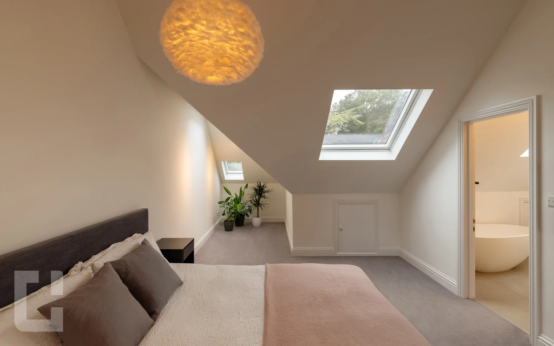 Loft bedroom with a large rooflight onto treetops and the en-suite bath visible through the door