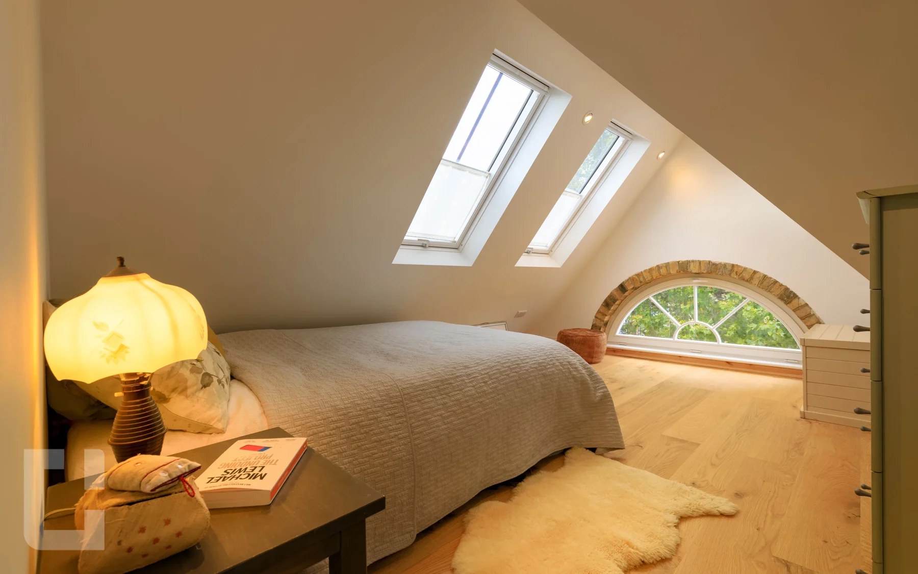 Loft bedroom looking past the bed to an arched gable window, with a sheepskin rug on oak boards