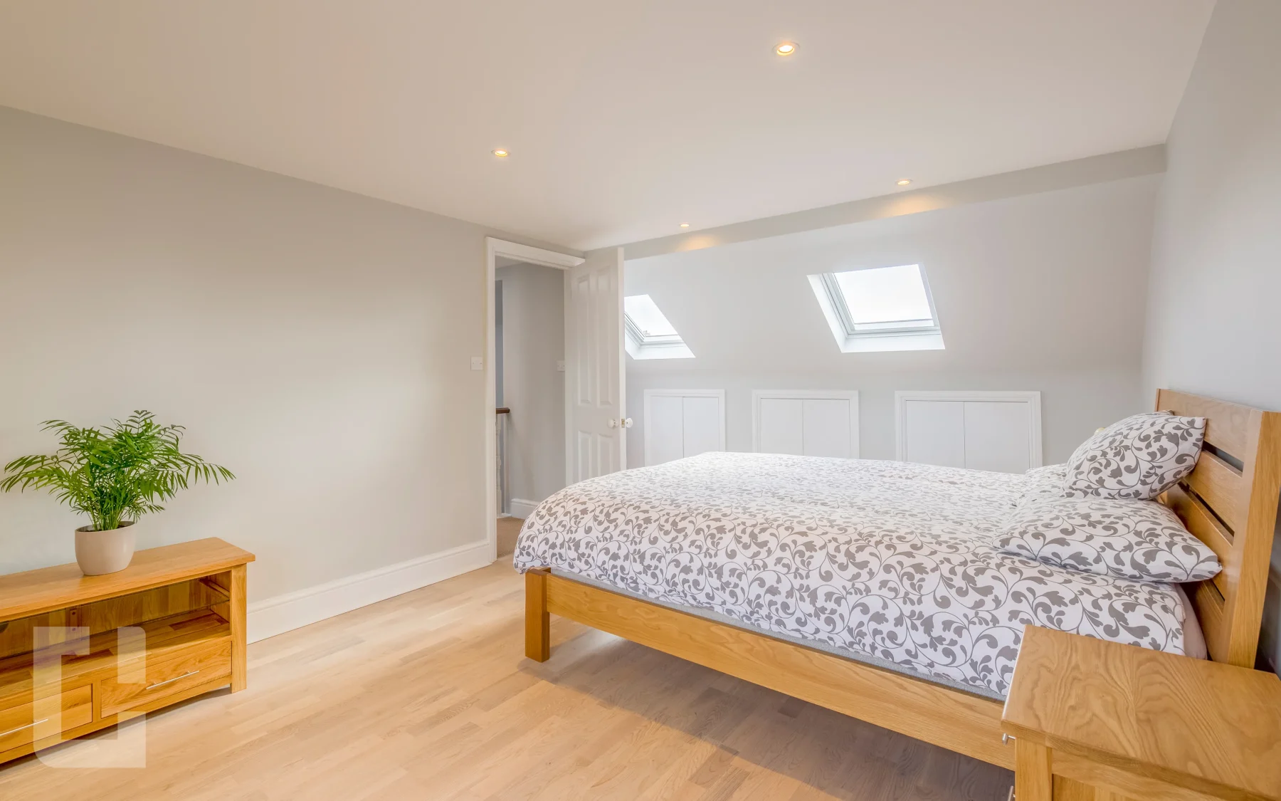 Spacious loft bedroom with two rooflights, fitted eaves cupboards and an oak bed