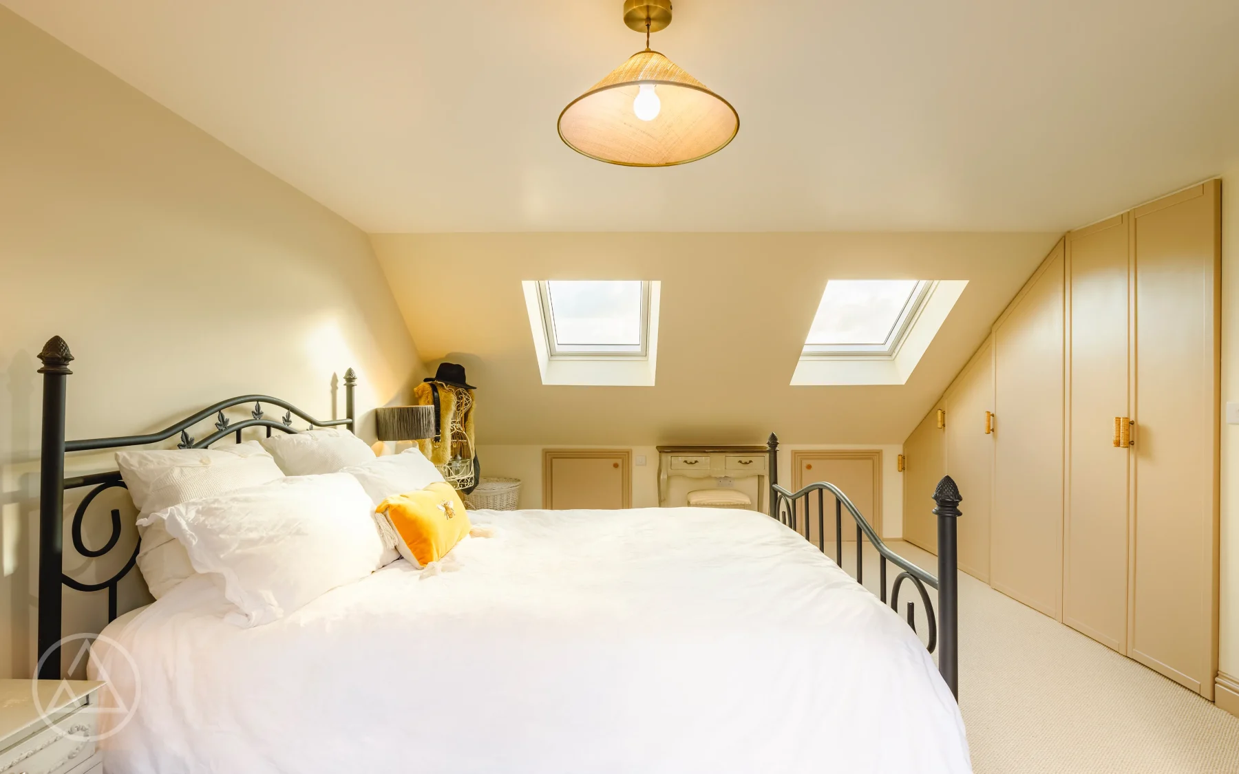 Loft bedroom with an iron bedstead, two rooflights and cream fitted eaves wardrobes