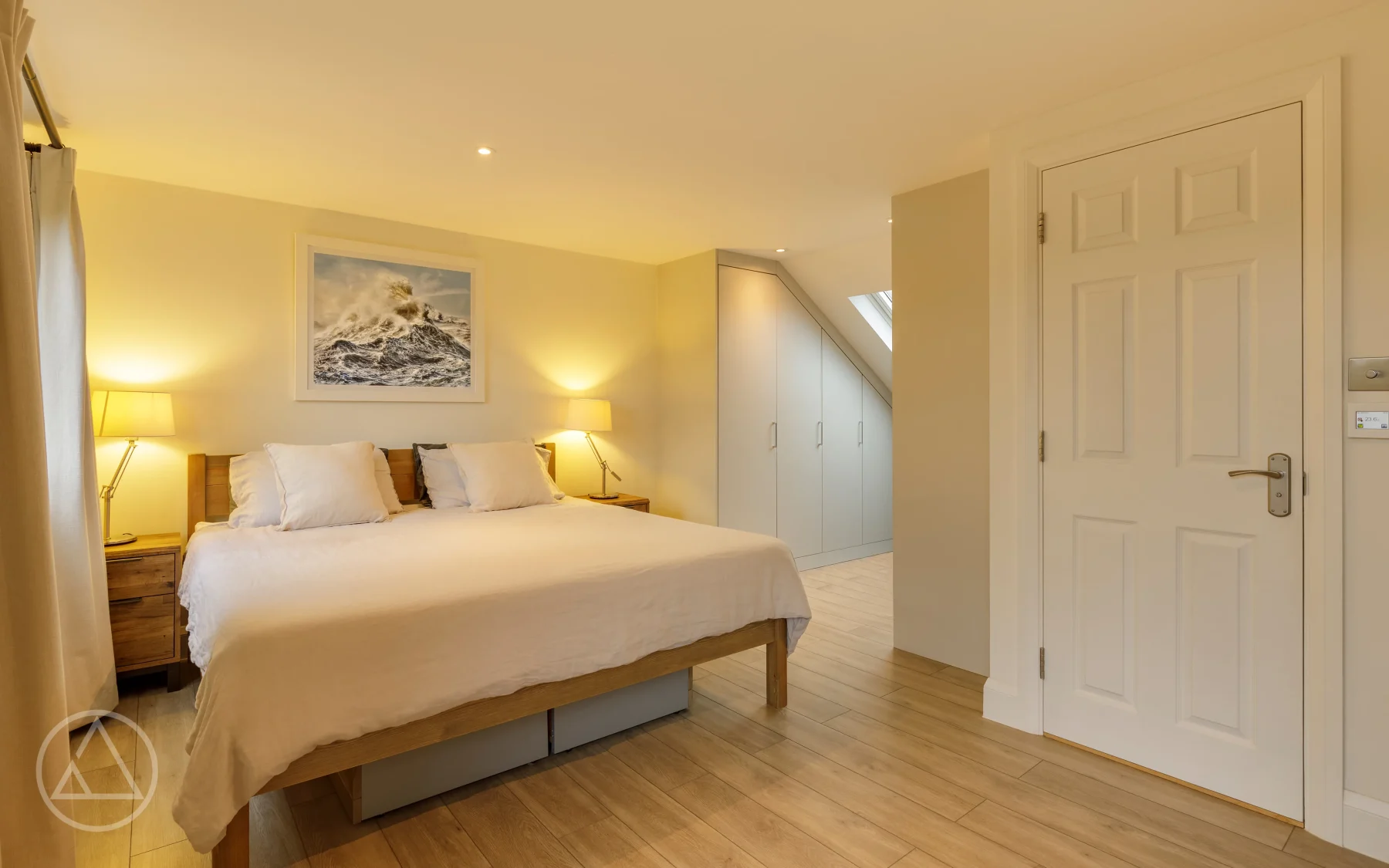 Loft master bedroom with an oak bed, bedside lamps and fitted wardrobes built into the eaves