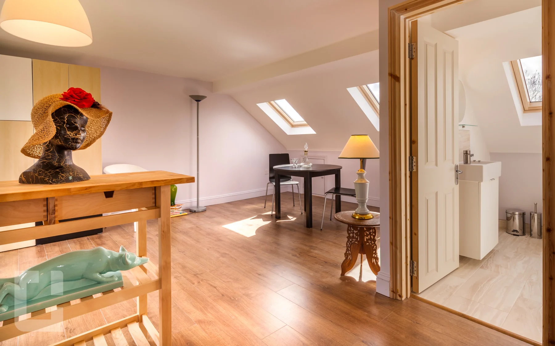 Open-plan loft room with sloping ceiling, rooflights and an open door to the loft bathroom