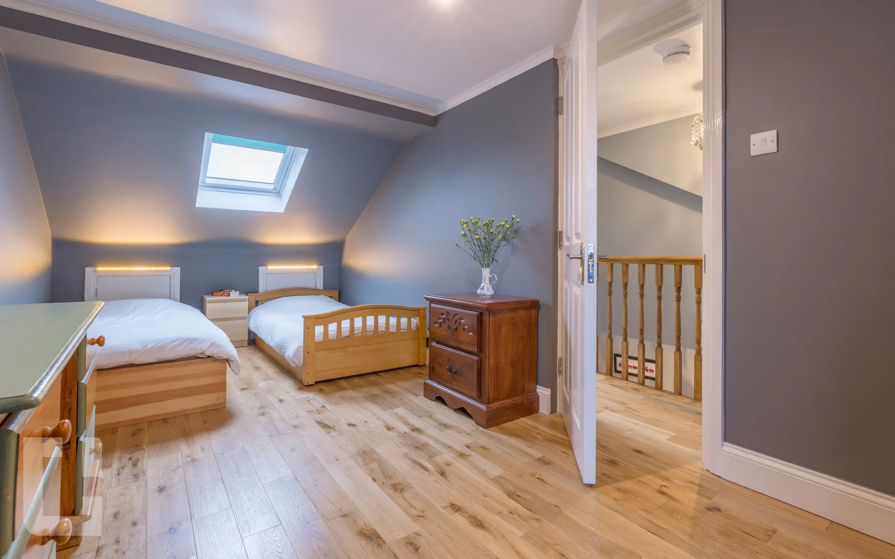 Twin loft bedroom with slate blue walls, oak flooring and a Velux rooflight in the ceiling slope